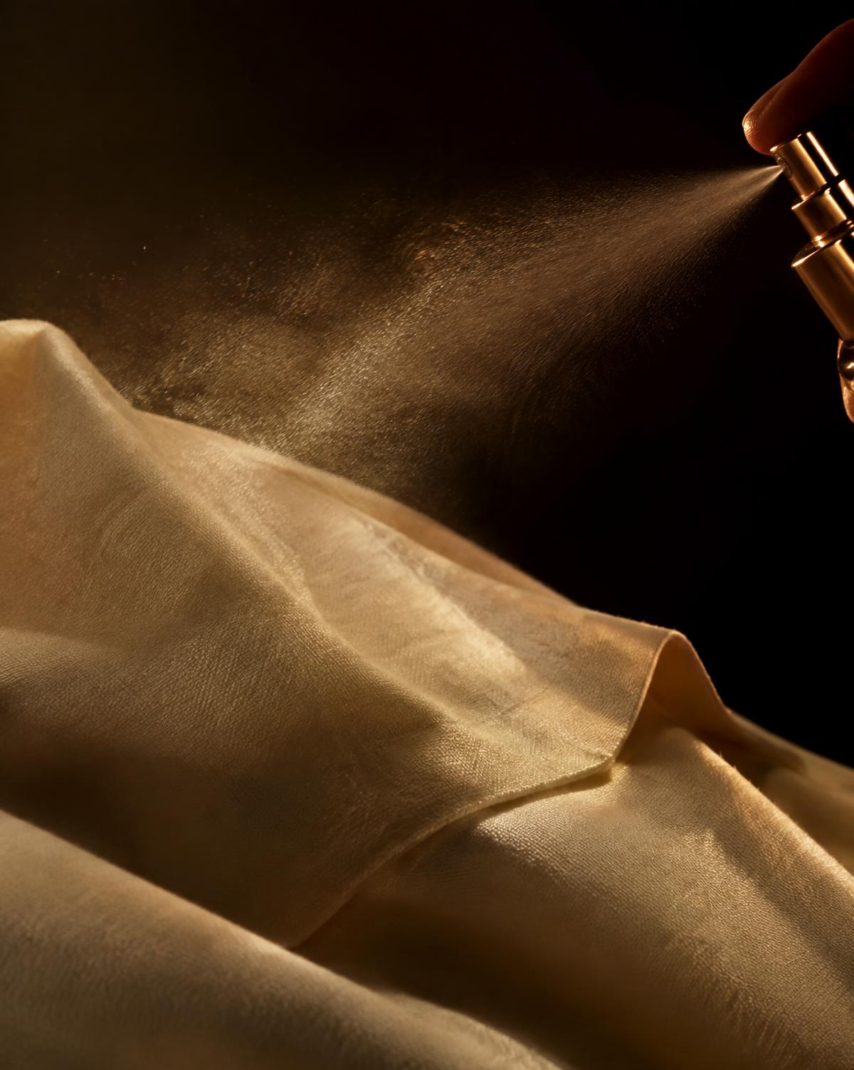 Apparel perfume being sprayed onto cream fabric